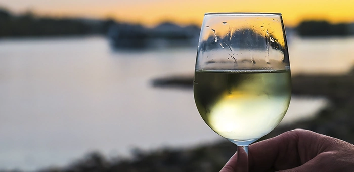 Ta&ccedil;a de vinho branco em fim de tarde &agrave; beira da &aacute;gua