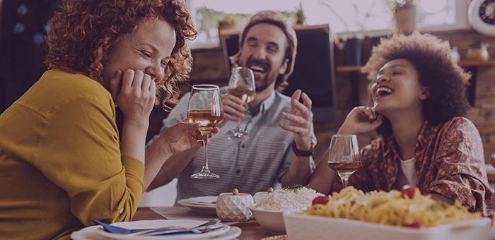 Amigos rindo em volta da mesa com ta&ccedil;as de vinho